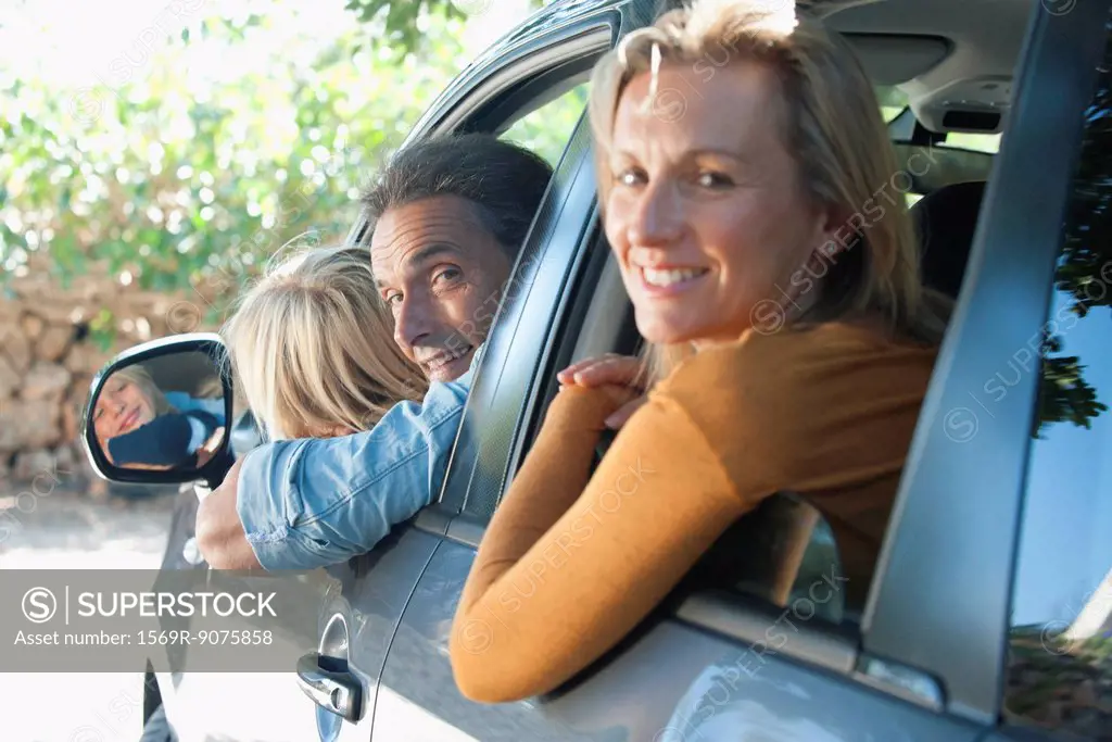 Family together in car, leaning out windows and smiling over shoulders at camera