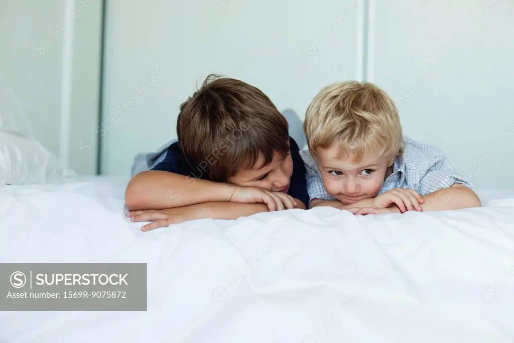 Young brothers lying on bed side by side, heads resting on arms