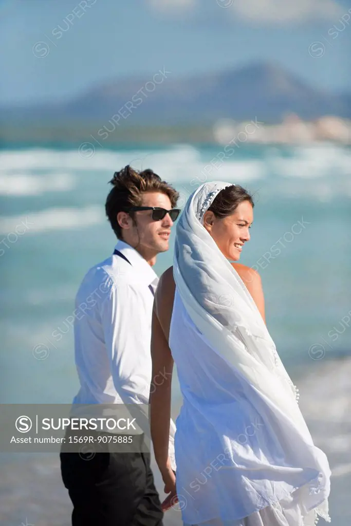 Bride and groom standing on beach, looking at view