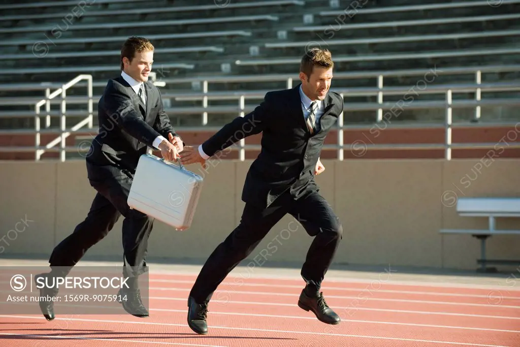 Businessmen running in relay race, handing off briefcase