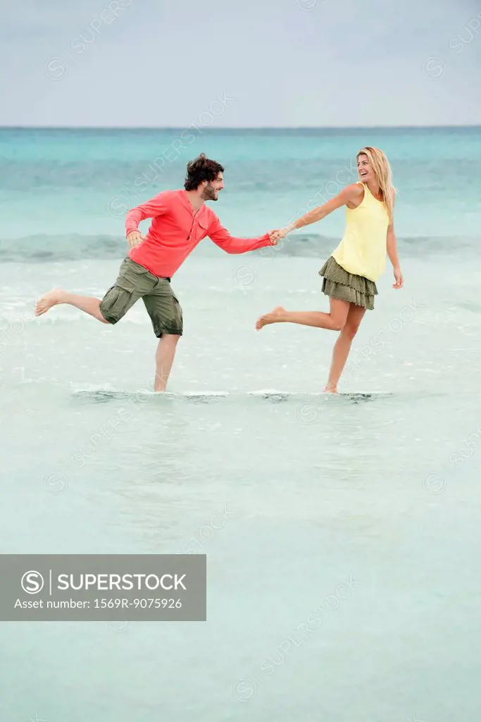 Couple standing on one leg in water at the beach, holding hands