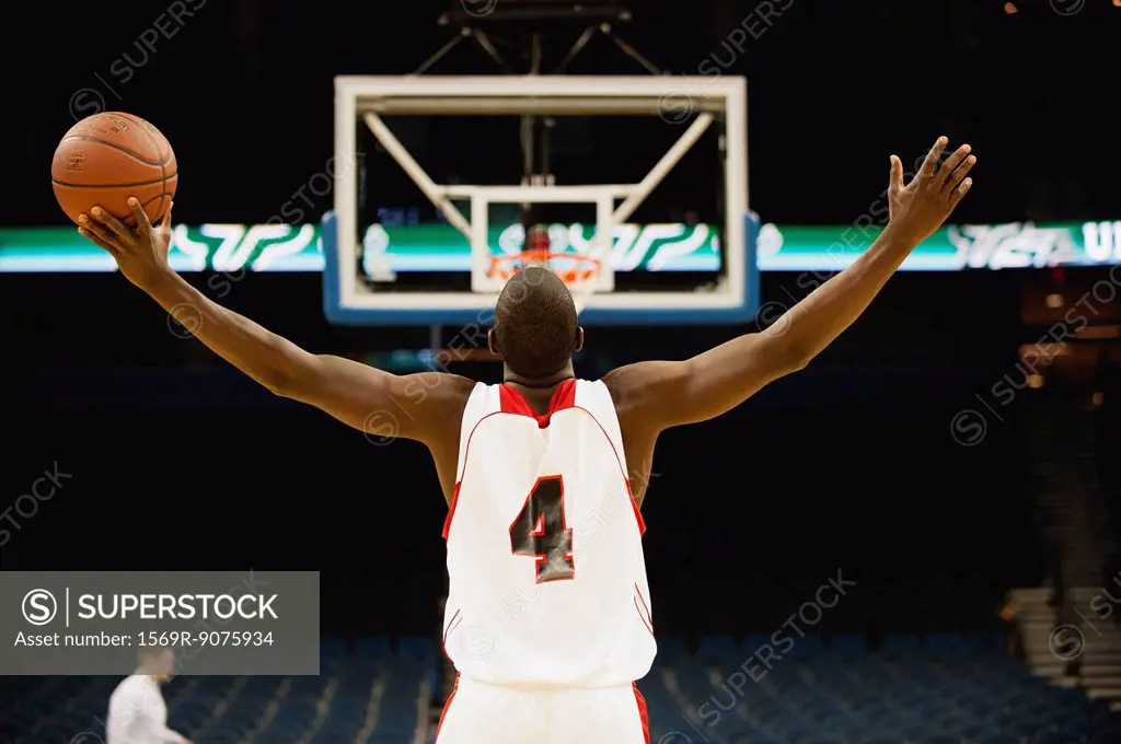 Basketball player standing in basketball court with arms outstretched, rear view