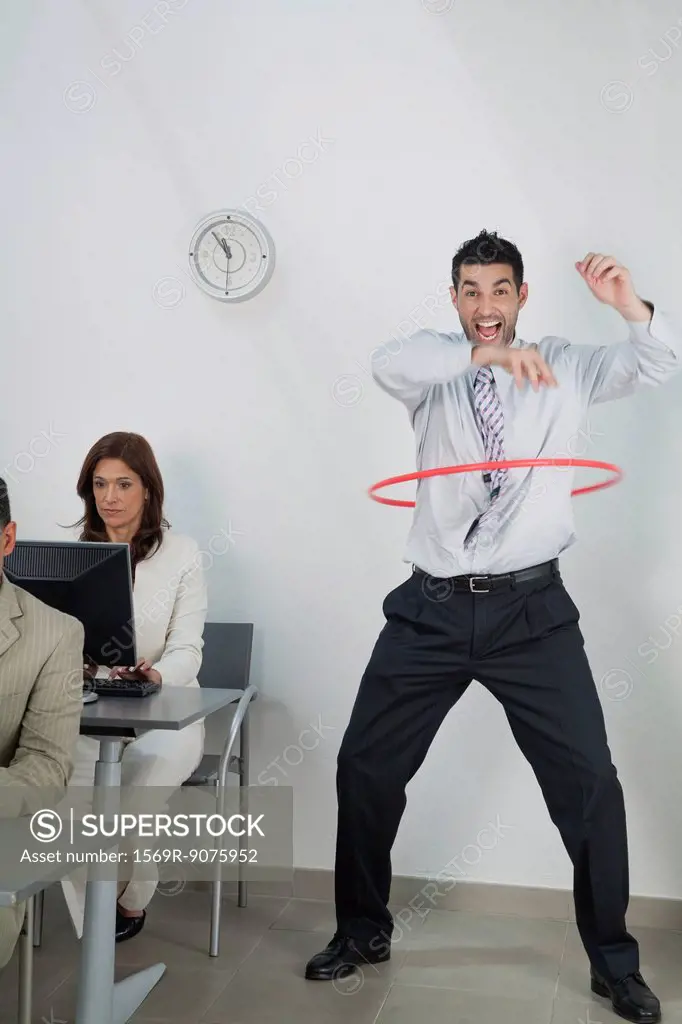 Young businessman playing with hula hoop in office while colleagues work