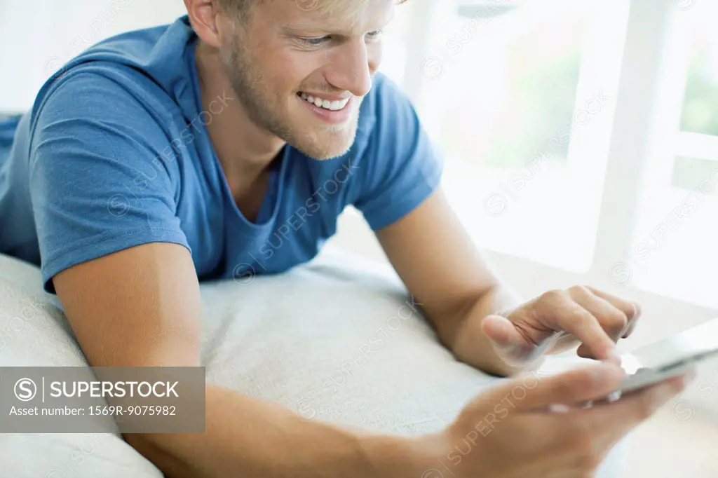 Man lying on stomach looking at digital tablet