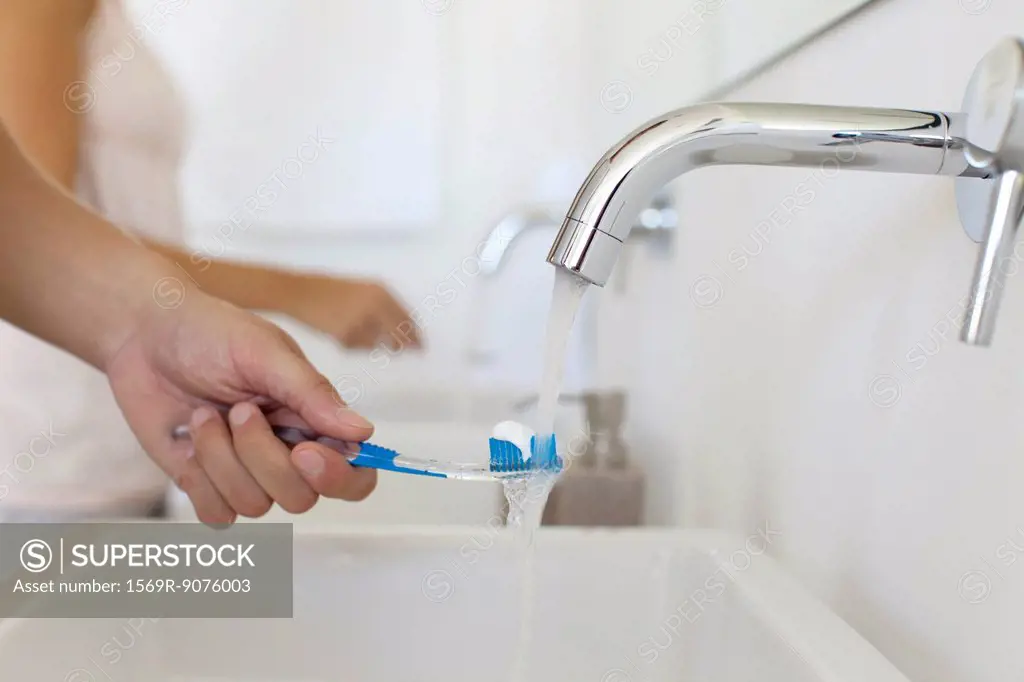 Man holding toothbrush under faucet, cropped