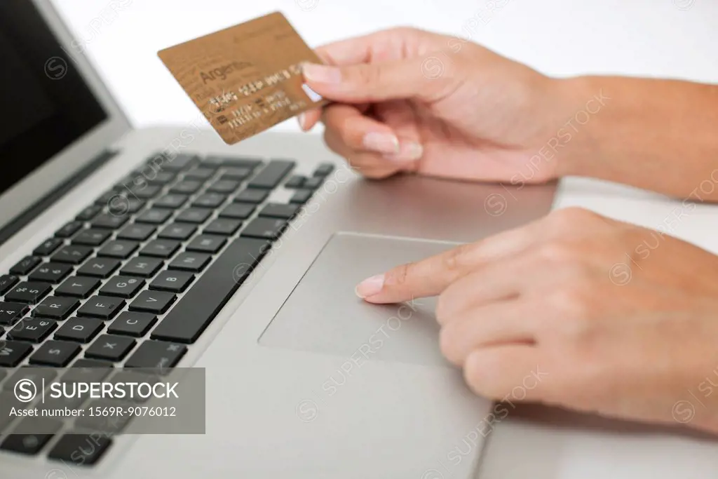 Woman holding credit card while using laptop computer, cropped