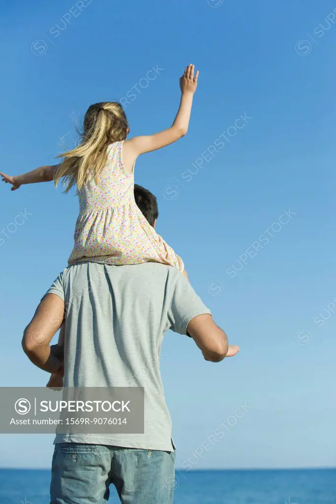 Father carrying daughter on his shoulders, rear view