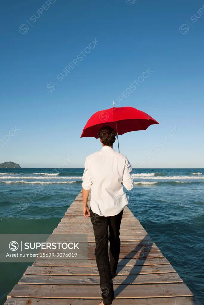 Man walking on pier with red umbrella, rear view