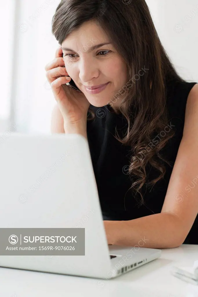 Mid_adult woman using cell phone and laptop
