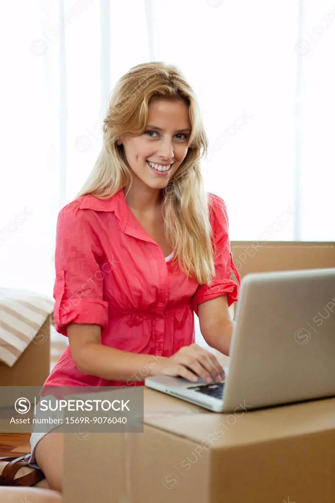 Young woman using laptop computer while surrounded by cardboard boxes