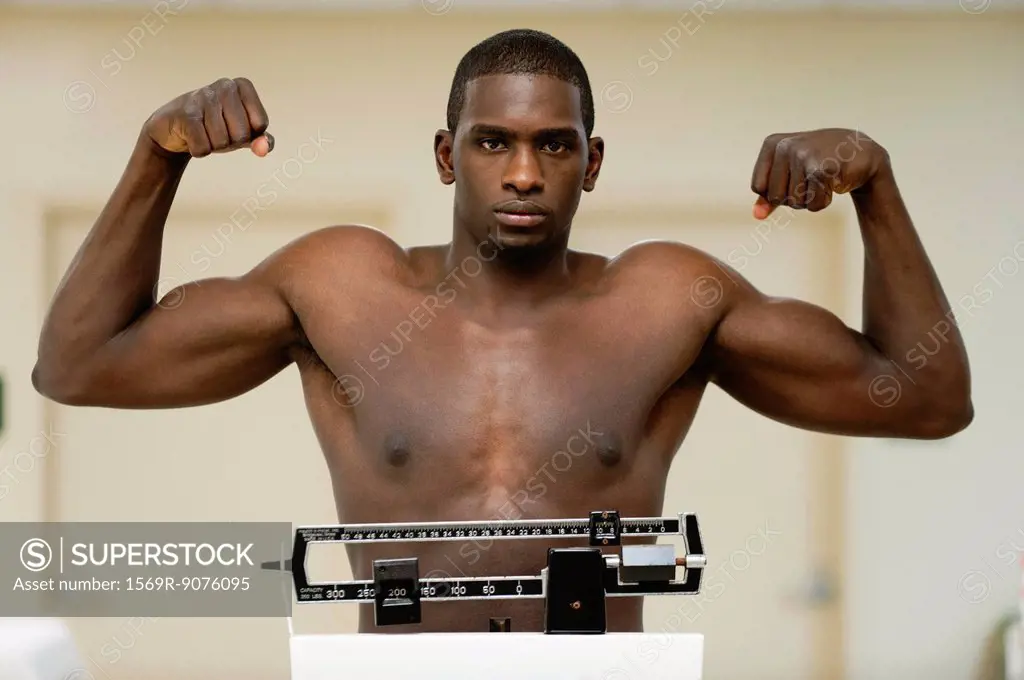 Young man flexing muscle on weight scale, portrait