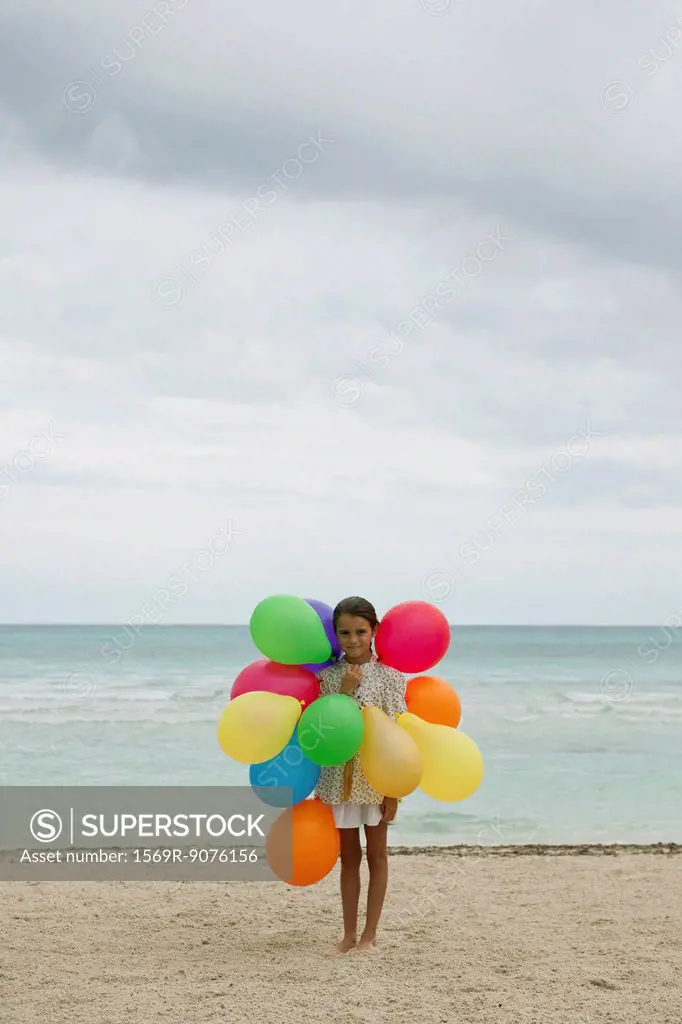 Girl with bunch of colorful balloons on beach
