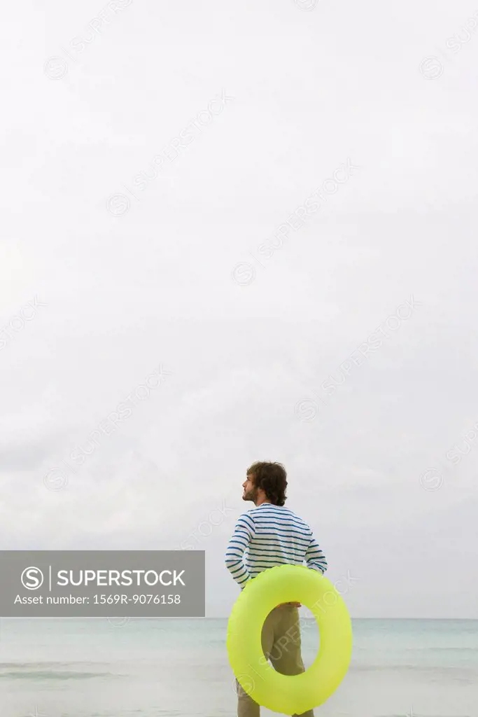 Young man holding inflatable ring, looking at ocean view