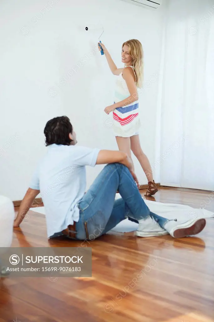 Man watching woman painting wall using paint roller