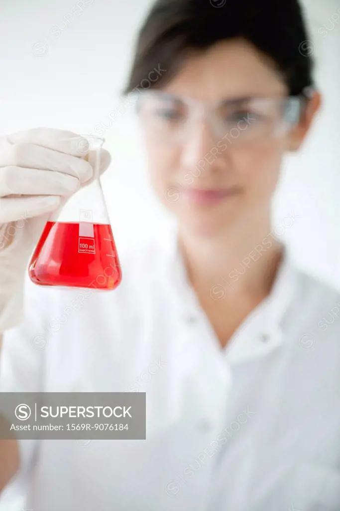 Scientist holding conical flask containing red liquid, focus on foreground