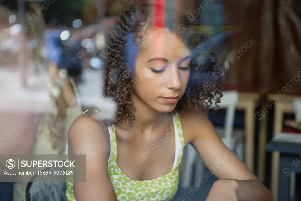 Young woman viewed through window, looking down in thought