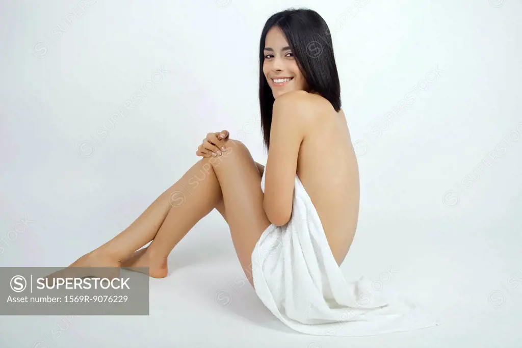 Nude woman partially covered with towel, smiling over shoulder at camera