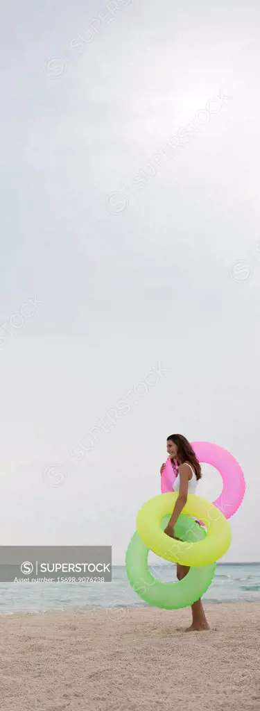 Woman standing on beach, holding inflatable rings, side view