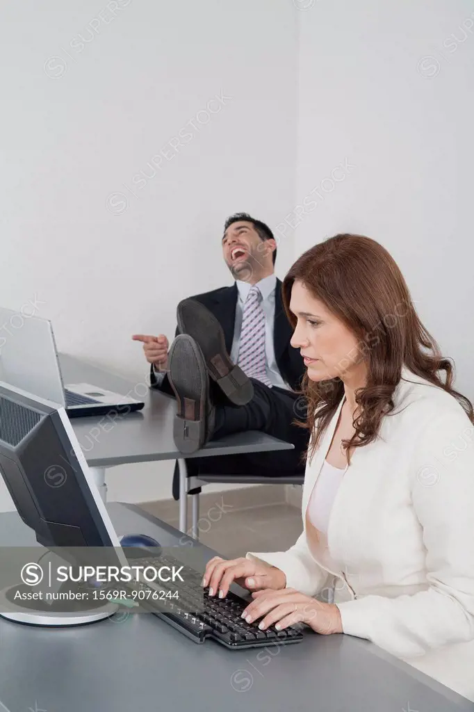 Businesswoman working in office while colleague laughs in background