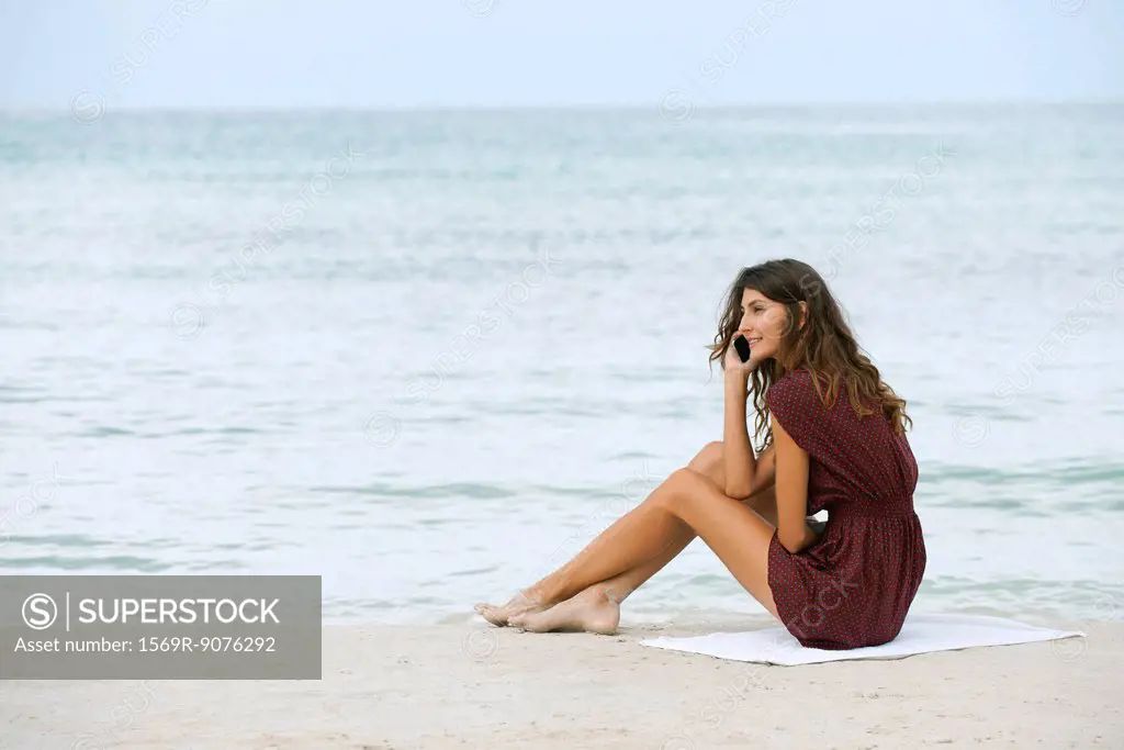 Young woman sitting on beach, using cell phone
