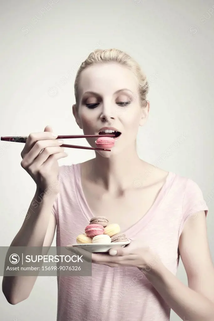 Young woman holding macaroon with chopsticks, portrait
