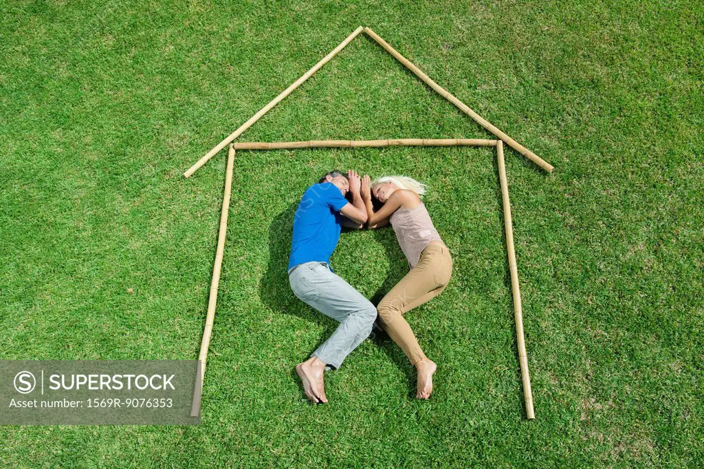 Couple lying on grass within outline of house, high angle view