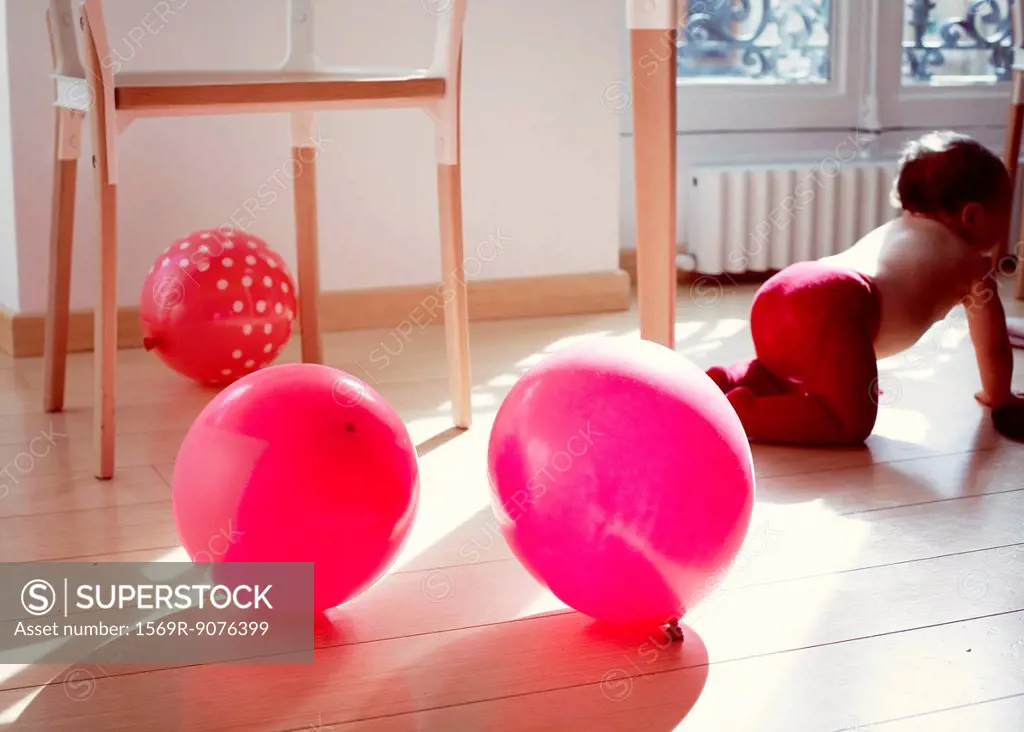 Infant crawling away from ballons on floor
