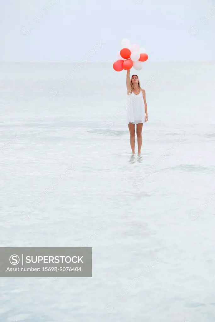 Woman standing on surface of water, holding bunch of balloons