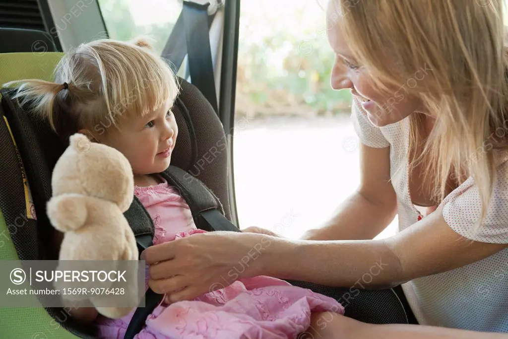 Mother fastening little girl into car seat