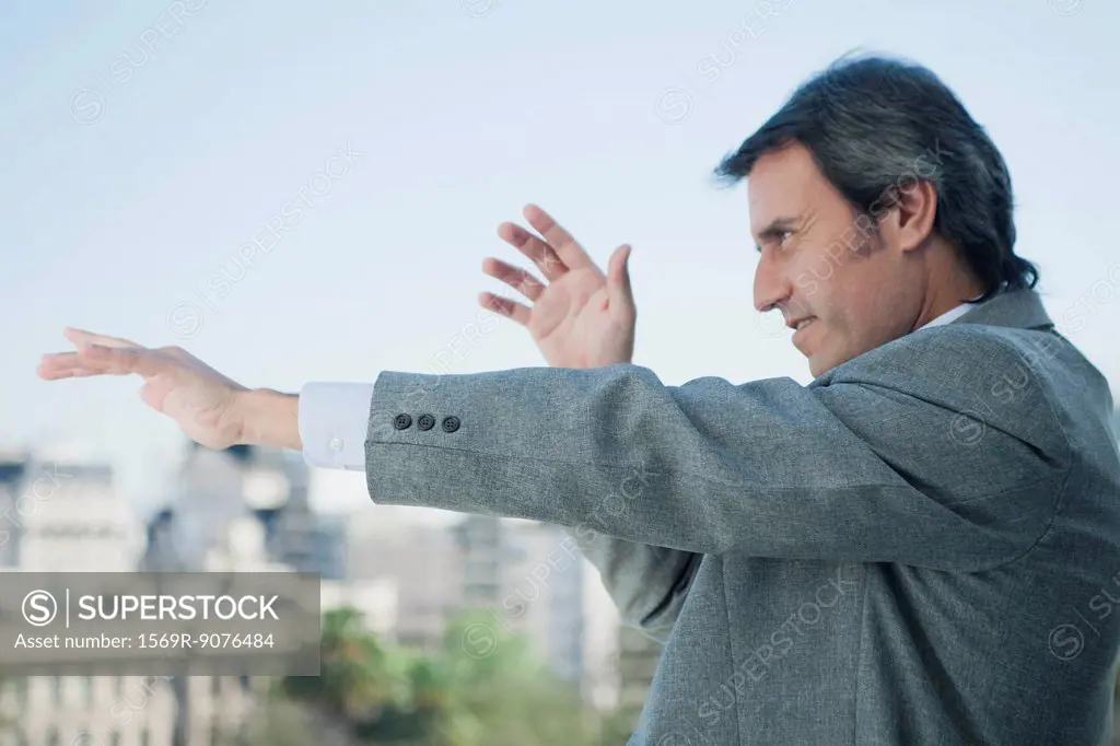 Mature businessman holding arms out in front of him and pointing, looking out of frame