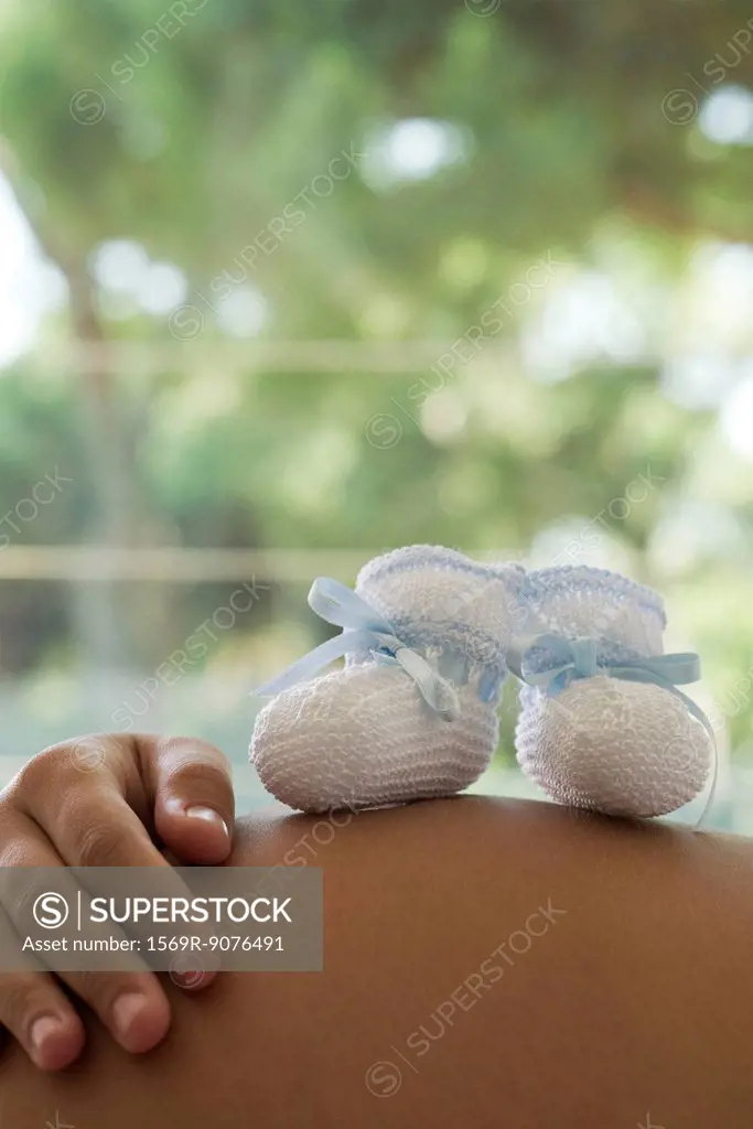 Baby booties resting on woman´s pregnant belly, cropped