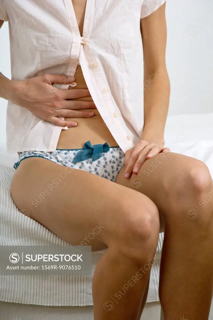 Woman sitting on bed, hand on stomach