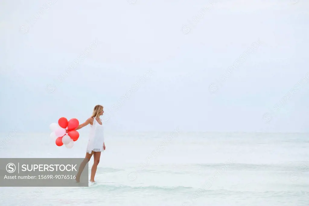 Woman walking on water, carrying bunch of balloons