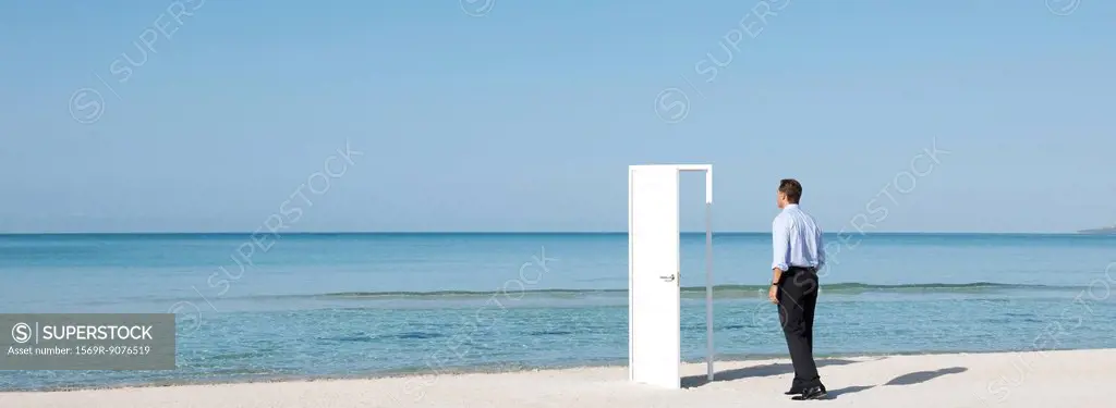 Businessman walking on beach towards open door, rear view