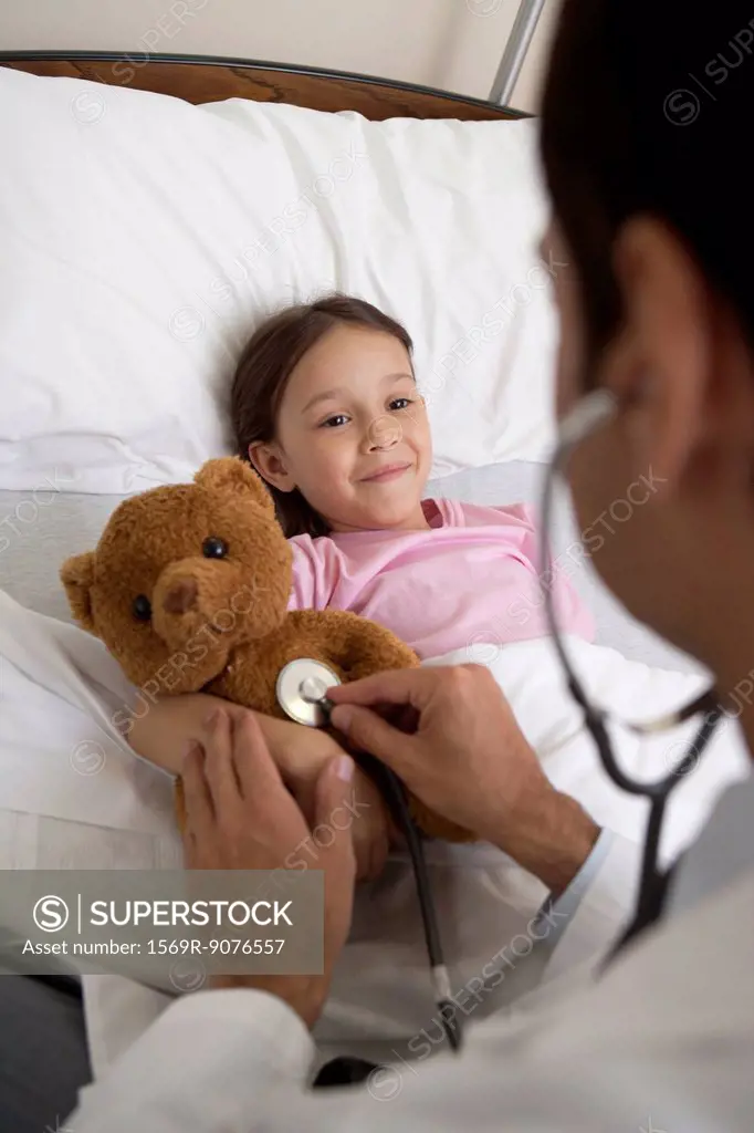 Doctor comforting young patient by examining her teddy bear with a stethoscope