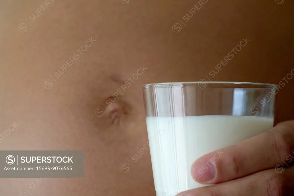 Pregnant woman holding glass of milk beside stomach, cropped