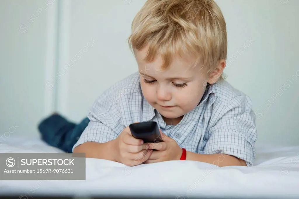 Little boy lying on bed holding cell phone