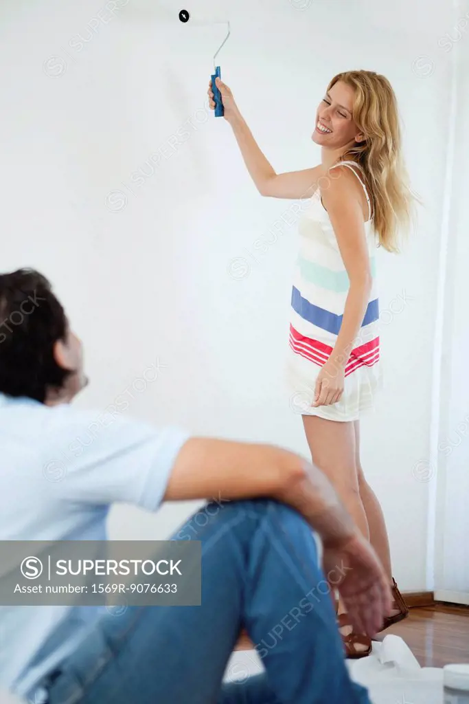 Young woman looking at husband while painting wall with paint roller