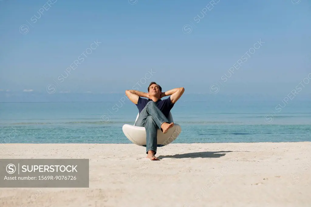 Mid_adult man relaxing in armchair on beach with eyes closed