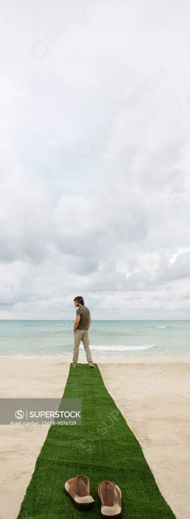 Man standing at end of carpet on beach, sandals on foreground