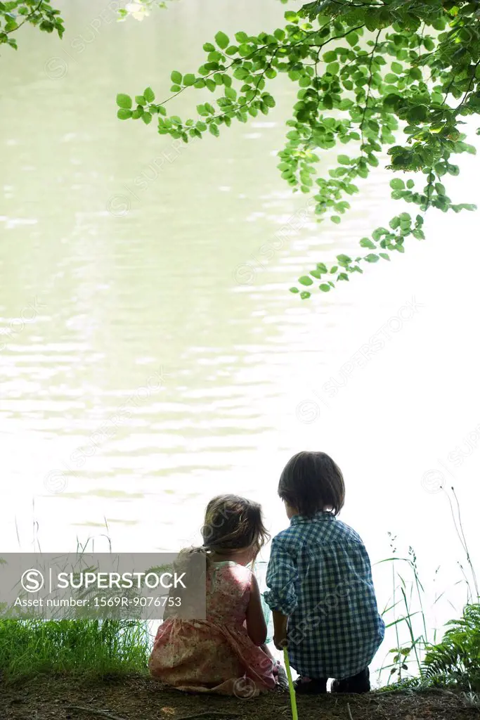 Children by lake with fish net, rear view, backlit