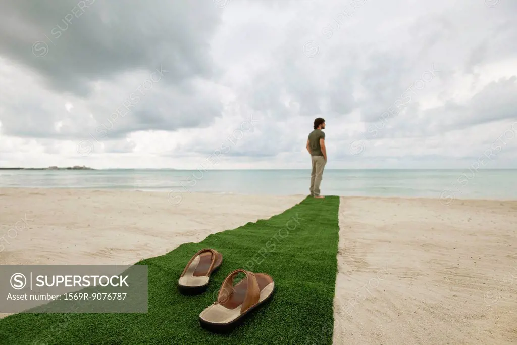 Man standing at end of carpet on beach, sandals on foreground