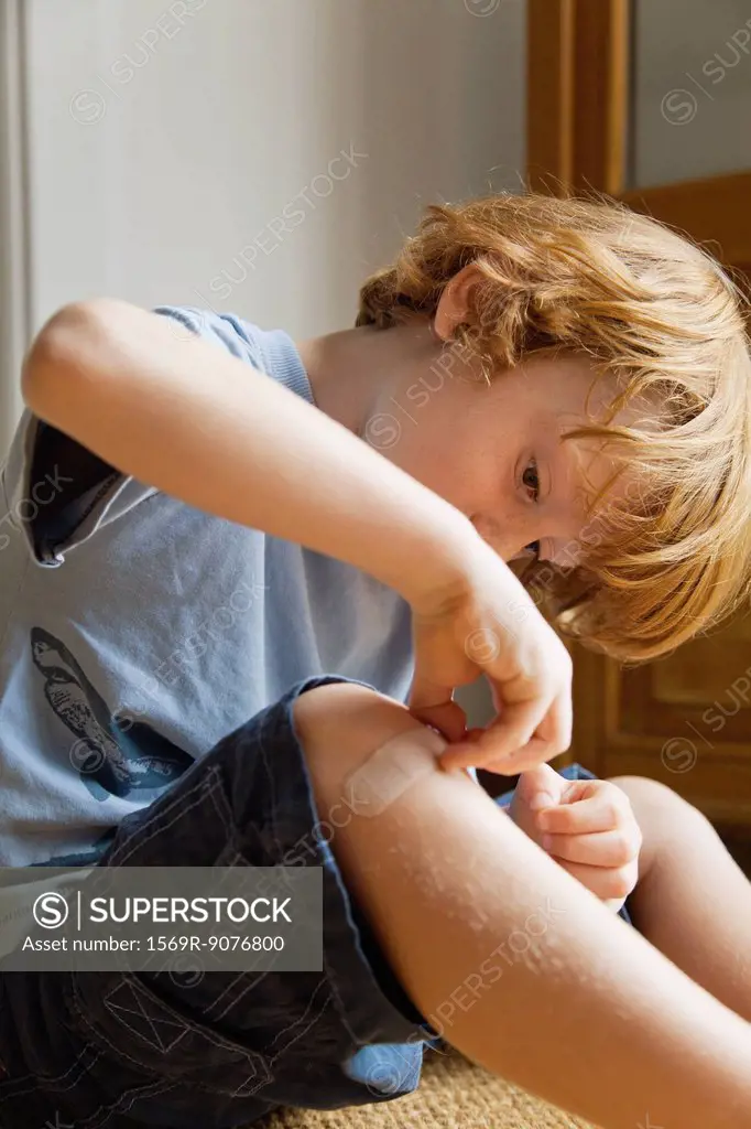 Boy removing adhesive bandage from knee