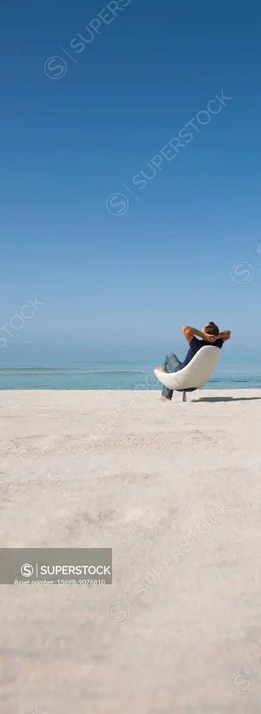 Man relaxing in chair on beach, rear view
