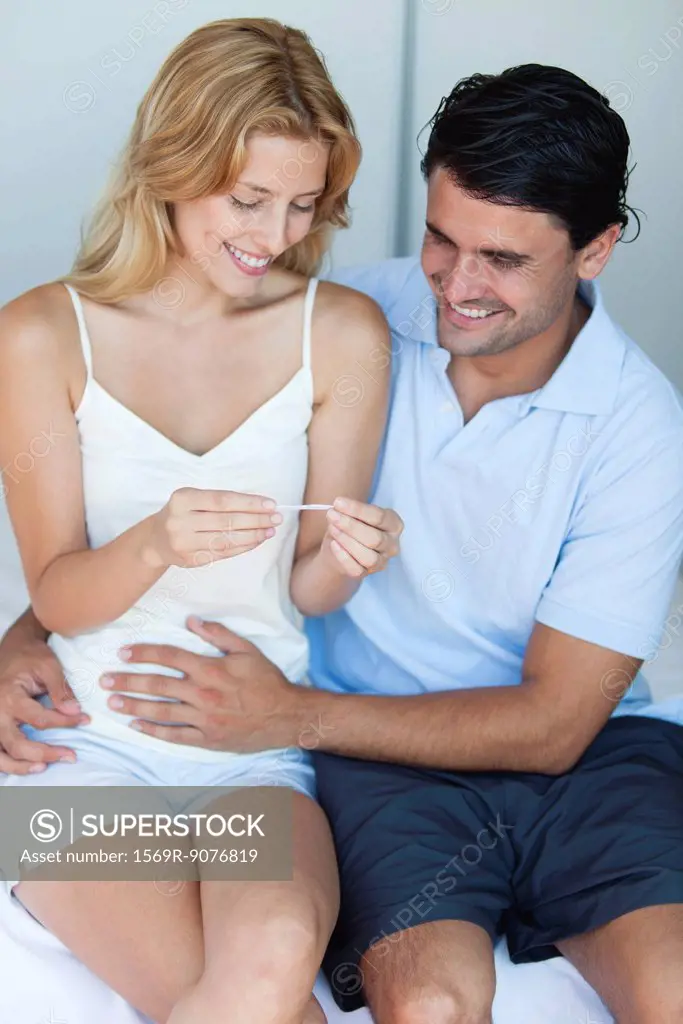 Couple looking at pregnancy test, man with hand on woman´s abdomen