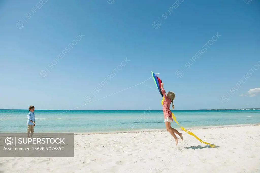 Boy flying kite on beach, girl jumping to catch