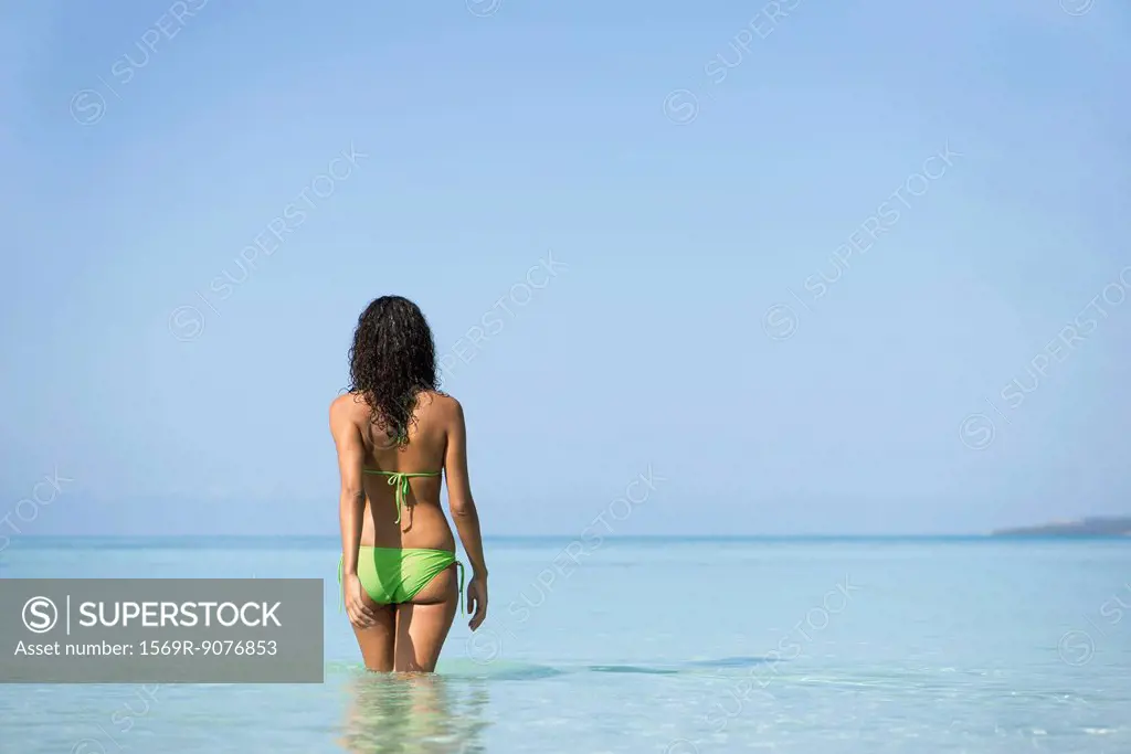 Woman in bikini walking in water, rear view