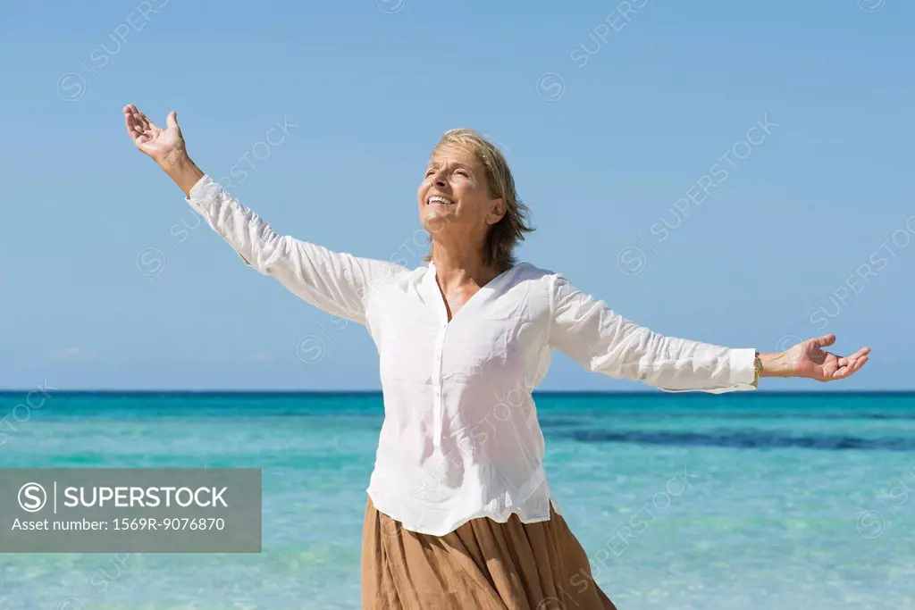 Senior woman by sea with arms outstretched, portrait