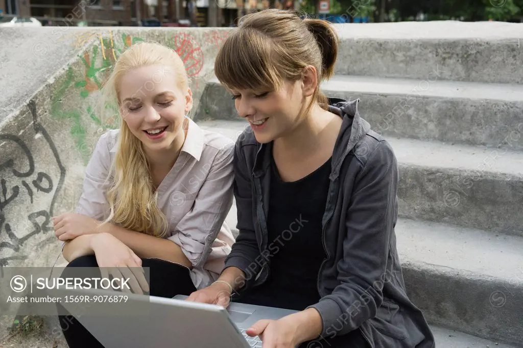 Young women looking at laptop computer together outdoors