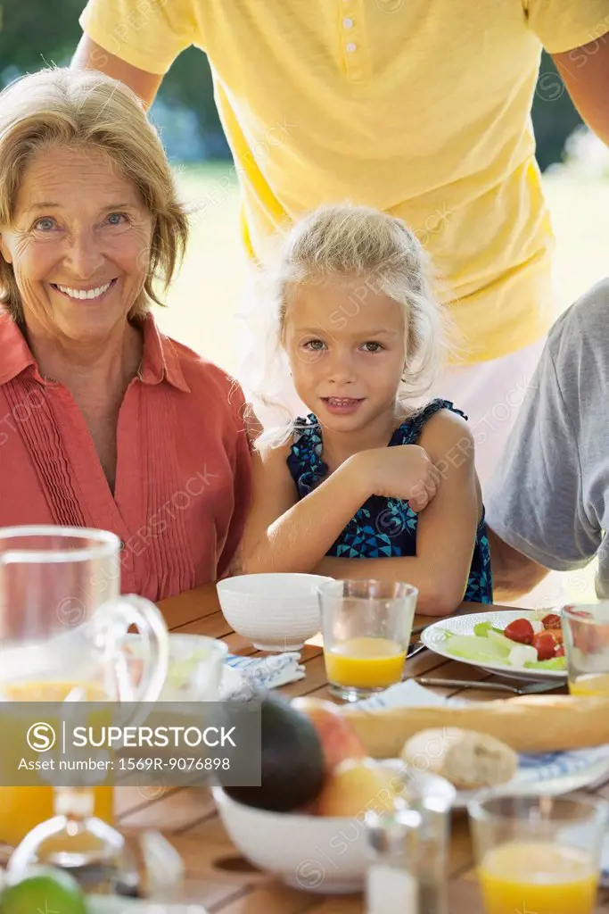 Girl and grandmother at breakfast table outdoors, cropped